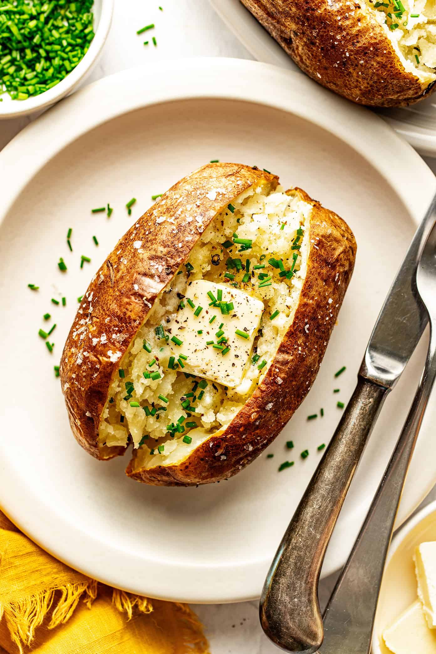 These air fryer baked potatoes turn out perfectly crisp on the outside and fluffy inside in under 45 minutes — the easiest way to make crisp baked potatoes without heating up your oven! | gimmesomeoven.com air fryer baked potato with butter and chives