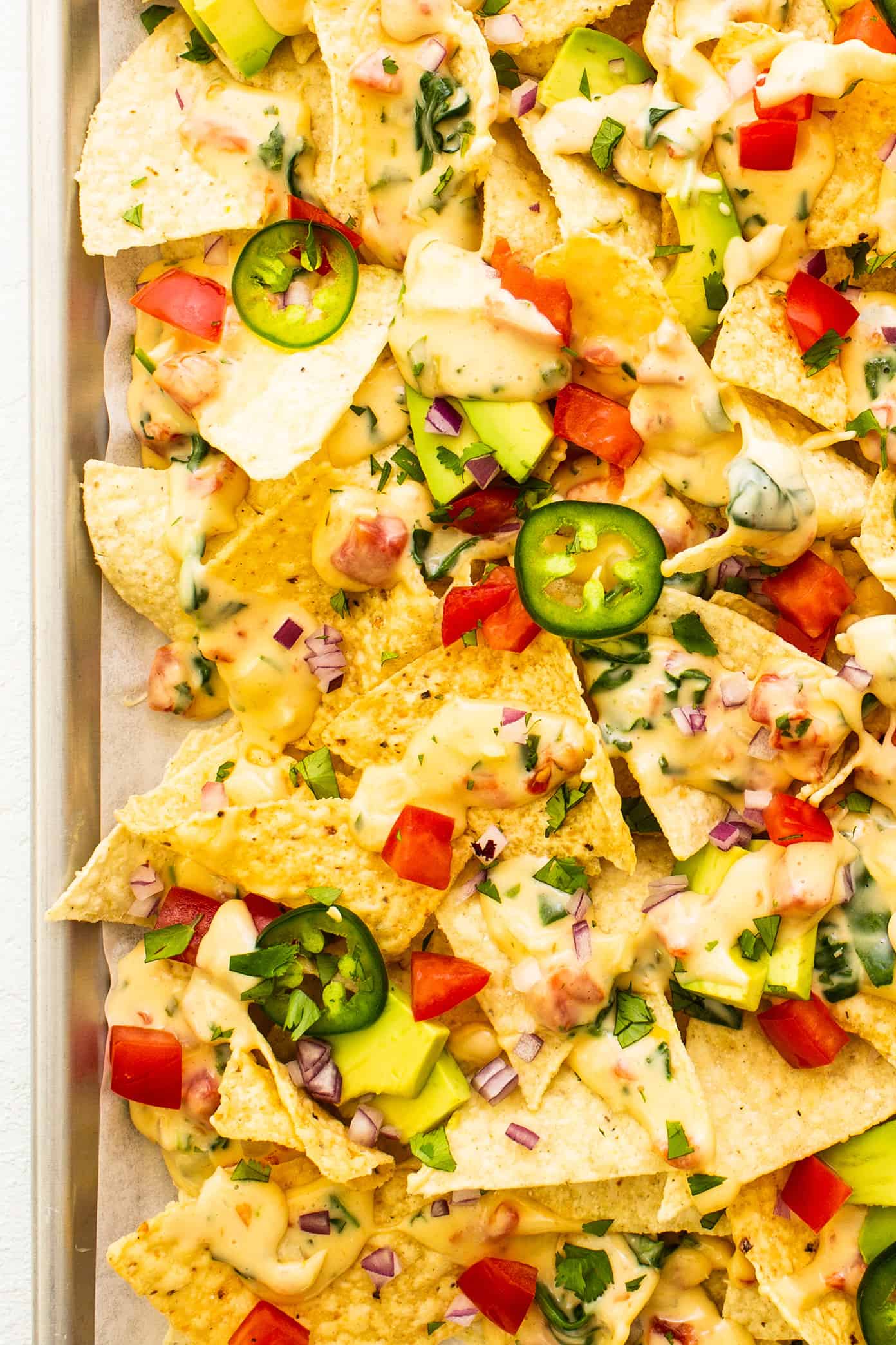 My go-to easy nachos recipe, made with my favorite Tex-Mex queso blanco dip, tortilla chips, avocado, tomato, red onion, jalapeรฑo and cilantro. Feel free to add meat, beans, salsa, or any other toppings that sound good too! | gimmesomeoven.com Favorite Easy Nachos with Queso Blanco on Sheet Pan