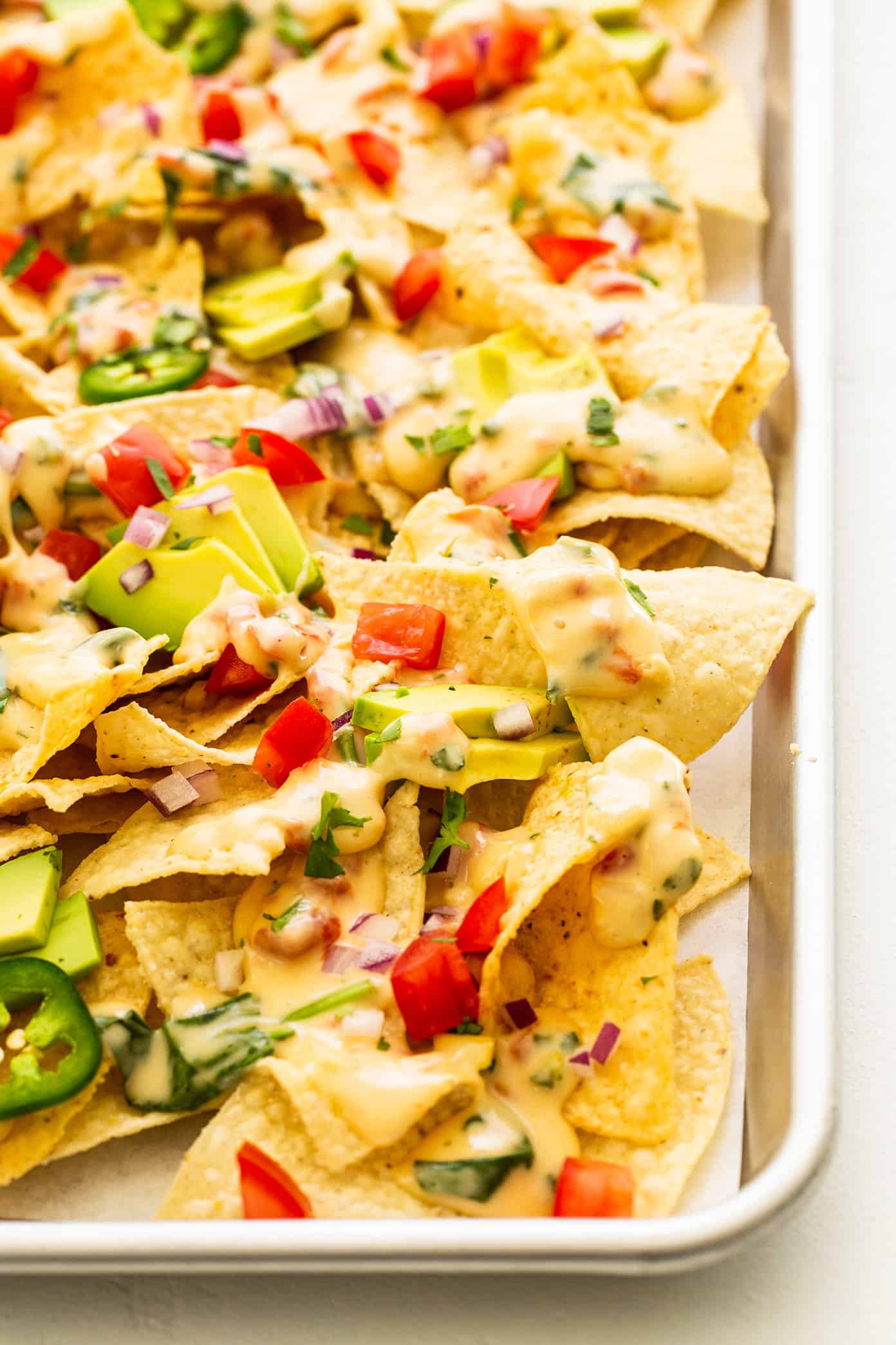 My go-to easy nachos recipe, made with my favorite Tex-Mex queso blanco dip, tortilla chips, avocado, tomato, red onion, jalapeรฑo and cilantro. Feel free to add meat, beans, salsa, or any other toppings that sound good too! | gimmesomeoven.com Easy Nachos in Sheet Pan with Avocado and Queso Blanco