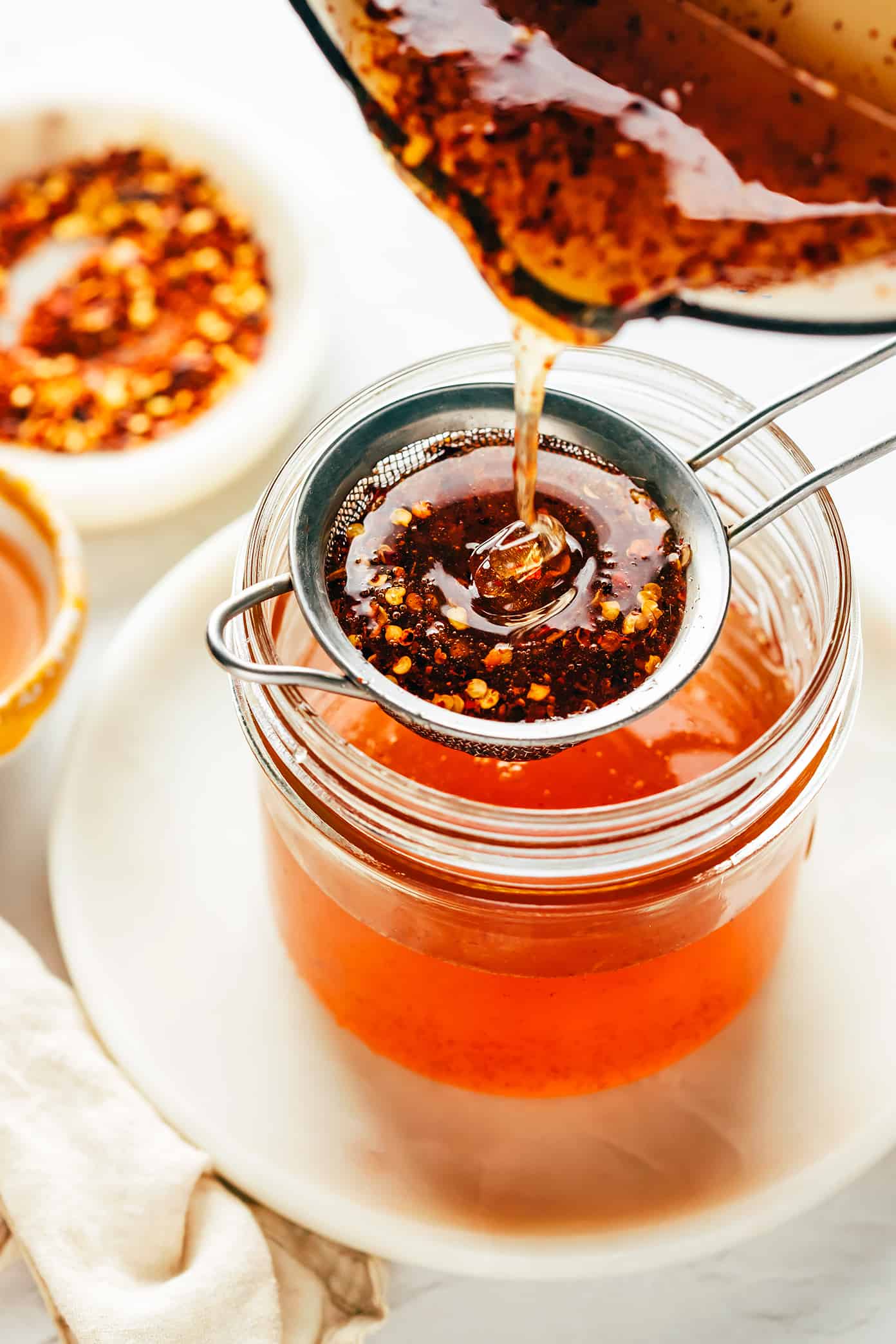 This homemade hot honey recipe is quick and easy to make with 3 ingredients and tastes delicious drizzled on everything from pizza to biscuits, fried chicken, salmon, veggies, baked brie and more! | gimmesomeoven.com Straining hot honey into jar