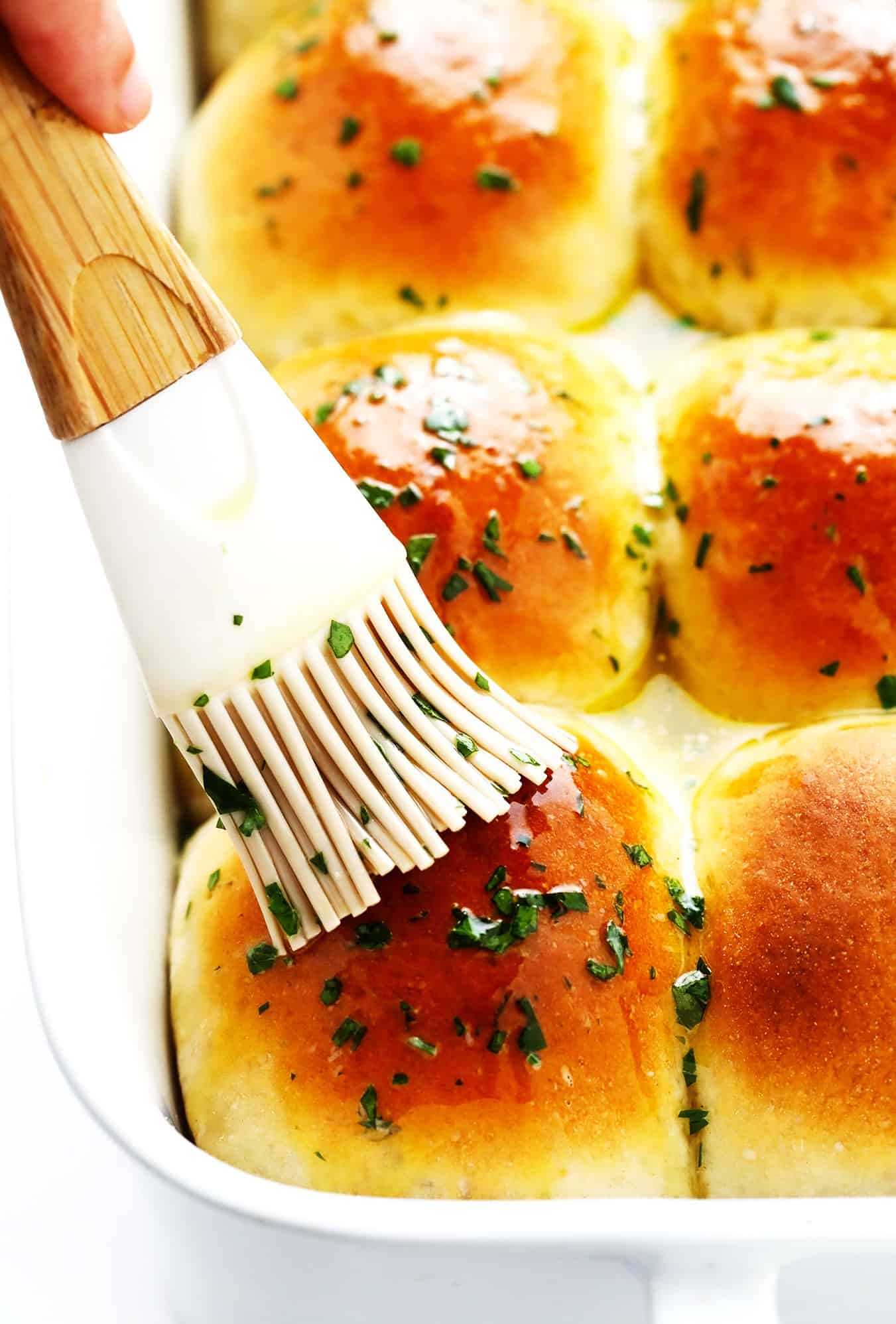 This rosemary garlic dinner rolls recipe is perfectly soft and fluffy, easy to make with or without a stand mixer, brushed with garlic herb butter and sprinkled with flaky sea salt, and ready to go in about one hour! Always a fantastic side dish for holidays like Thanksgiving, or the perfect easy bread recipe for weeknight dinners too. Vegan option included. | gimmesomeoven.com Brushing dinner rolls with garlic butter