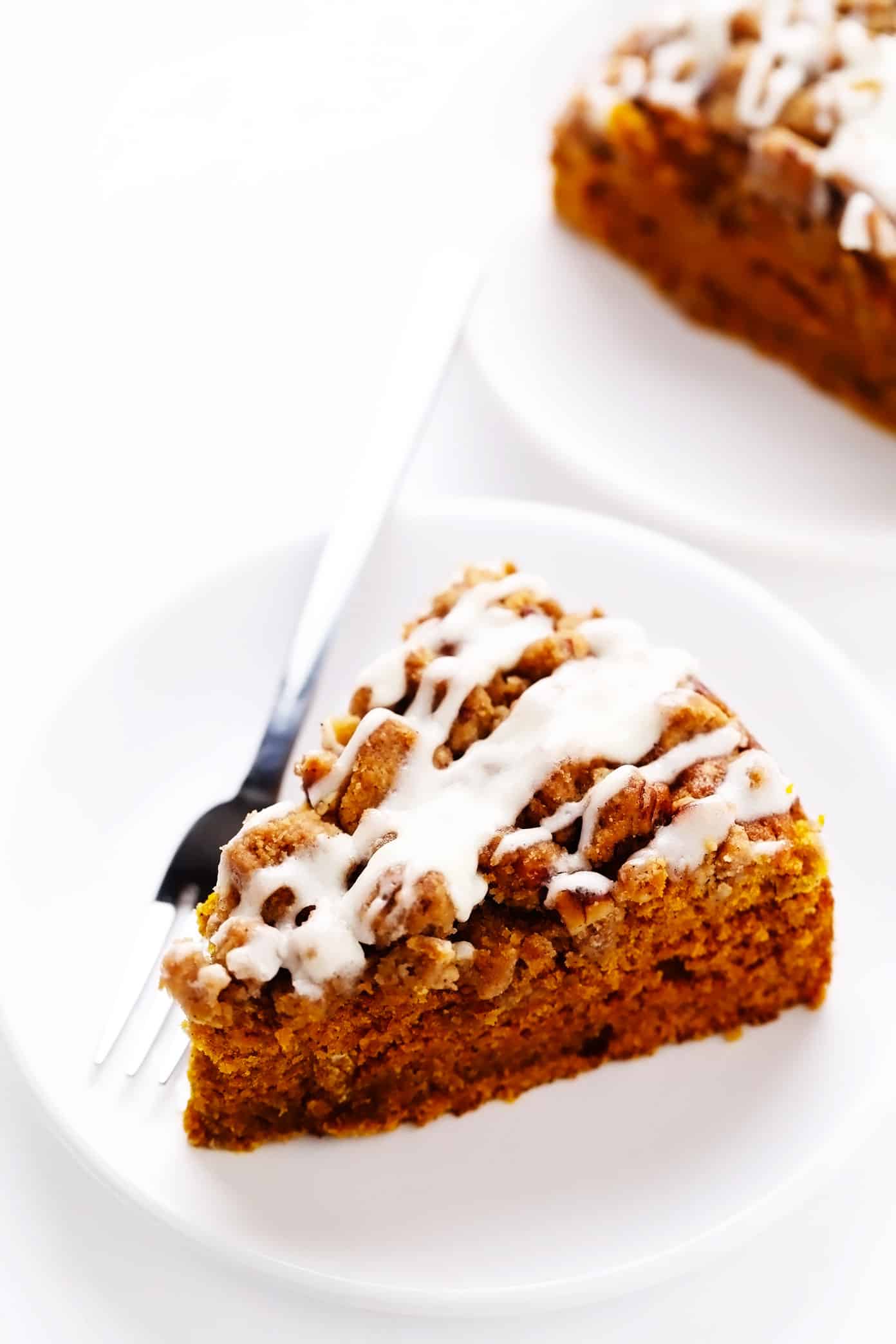 This pumpkin coffee cake is moist and perfectly spiced, then topped with a crunchy streusel crumb topping and a quick cream cheese drizzle. It's easy to make and the perfect breakfast or brunch treat for fall or the holidays! | gimmesomeoven.com Serving pieces of pumpkin coffee cake with streusel and cream cheese icing