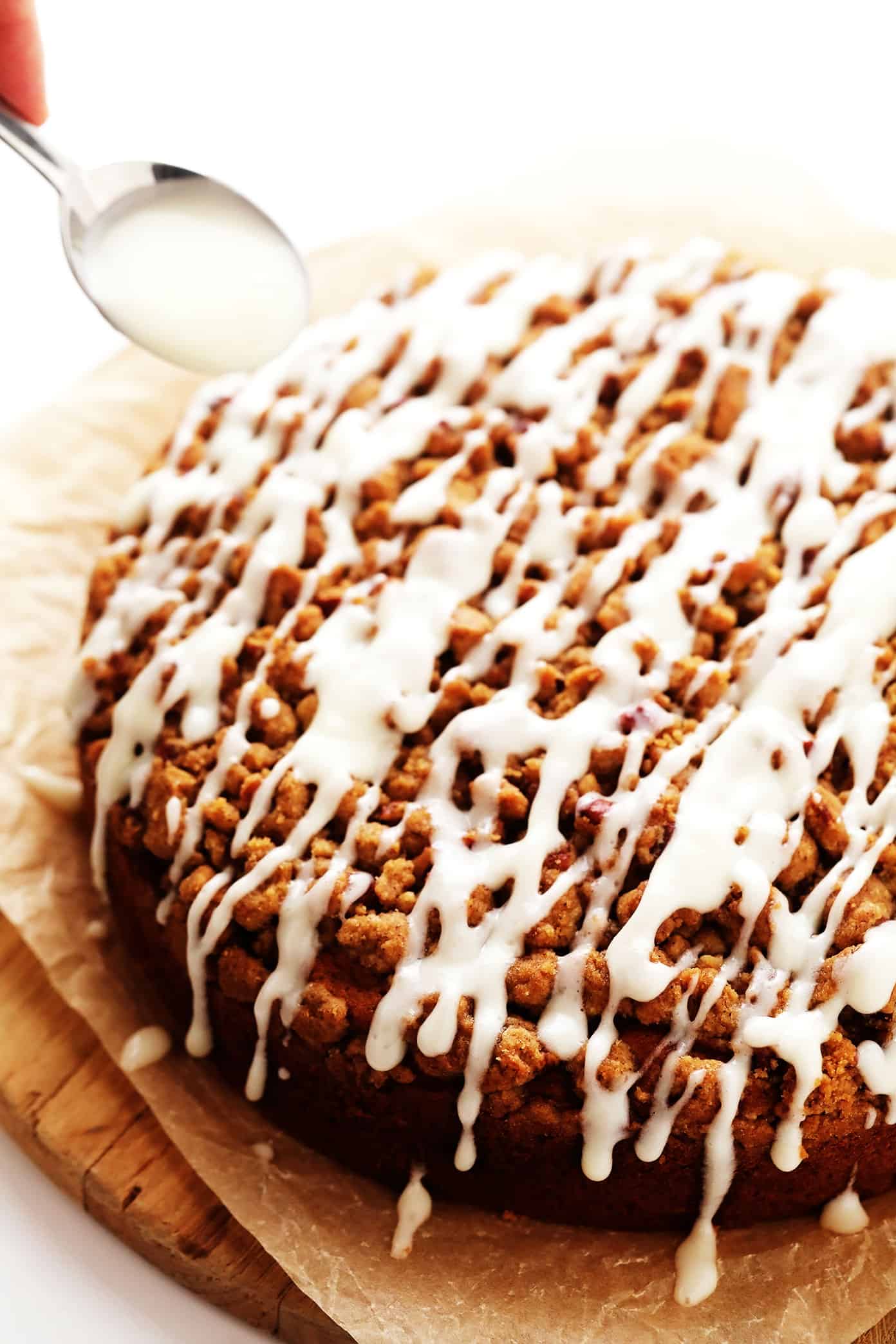 This pumpkin coffee cake is moist and perfectly spiced, then topped with a crunchy streusel crumb topping and a quick cream cheese drizzle. It's easy to make and the perfect breakfast or brunch treat for fall or the holidays! | gimmesomeoven.com Drizzling cream cheese icing on pumpkin crumb cake