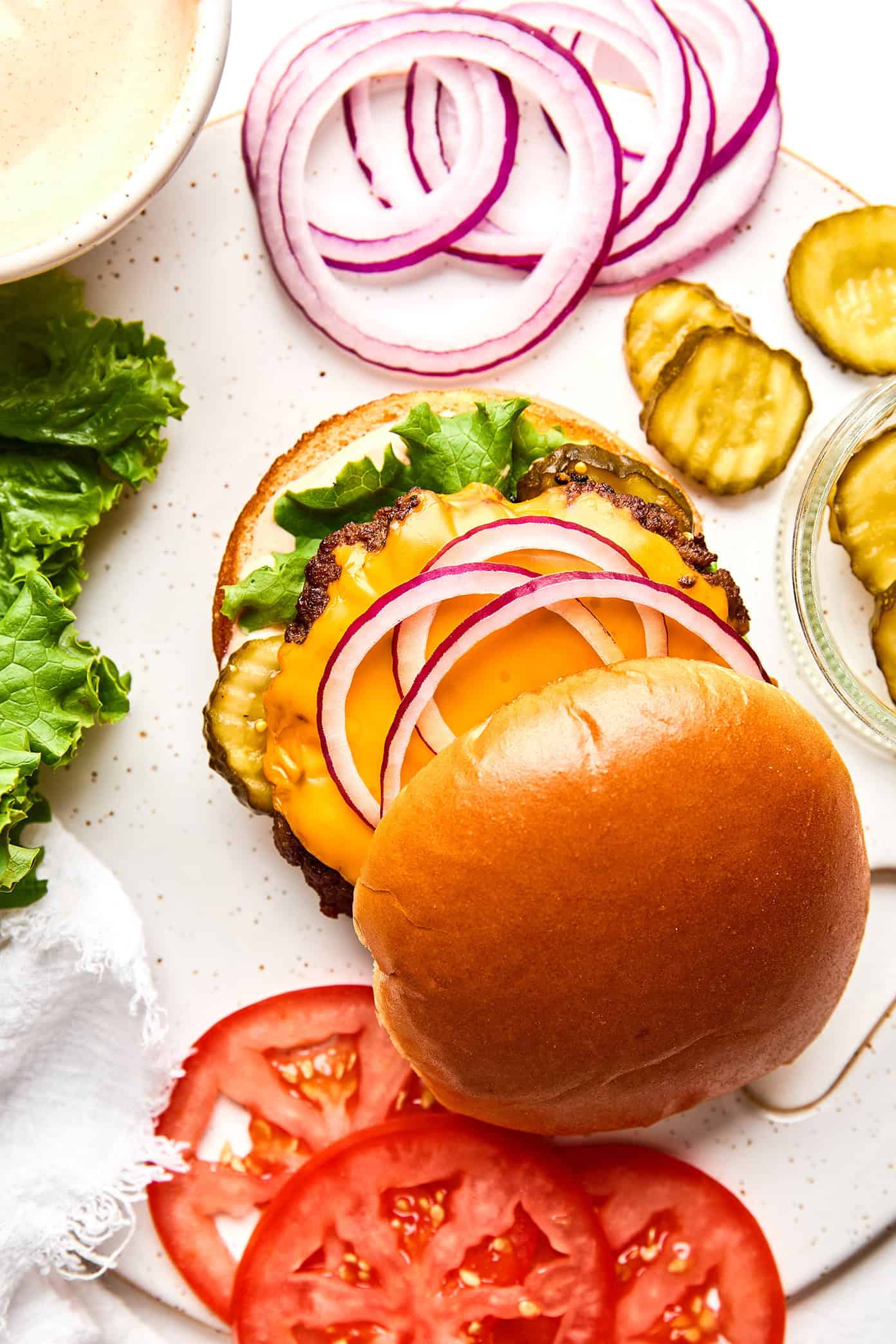 Learn how to make the most juicy, crispy-edged, flavorful homemade smash burgers with this quick and easy recipe. Perfect for easy dinners, grill outs, game day, or anytime you're craving an excellent burger. | gimmesomeoven.com Layering a smash burger with toppings