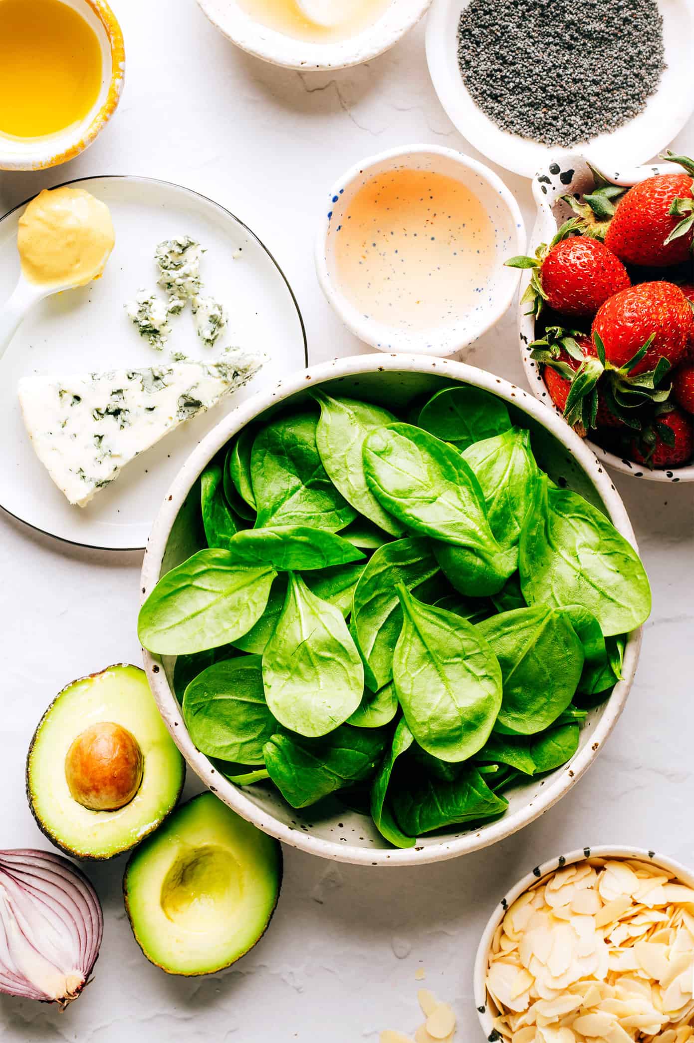 This fresh strawberry spinach salad recipe is tossed with creamy avocado, toasted almonds, sliced red onion, your choice of cheese (blue, feta, goat) and a lightly-sweetened honey poppyseed dressing. Feel free to add in some grilled chicken, shrimp or bacon if you'd like too! | gimmesomeoven.com Strawberry Spinach Salad Ingredients