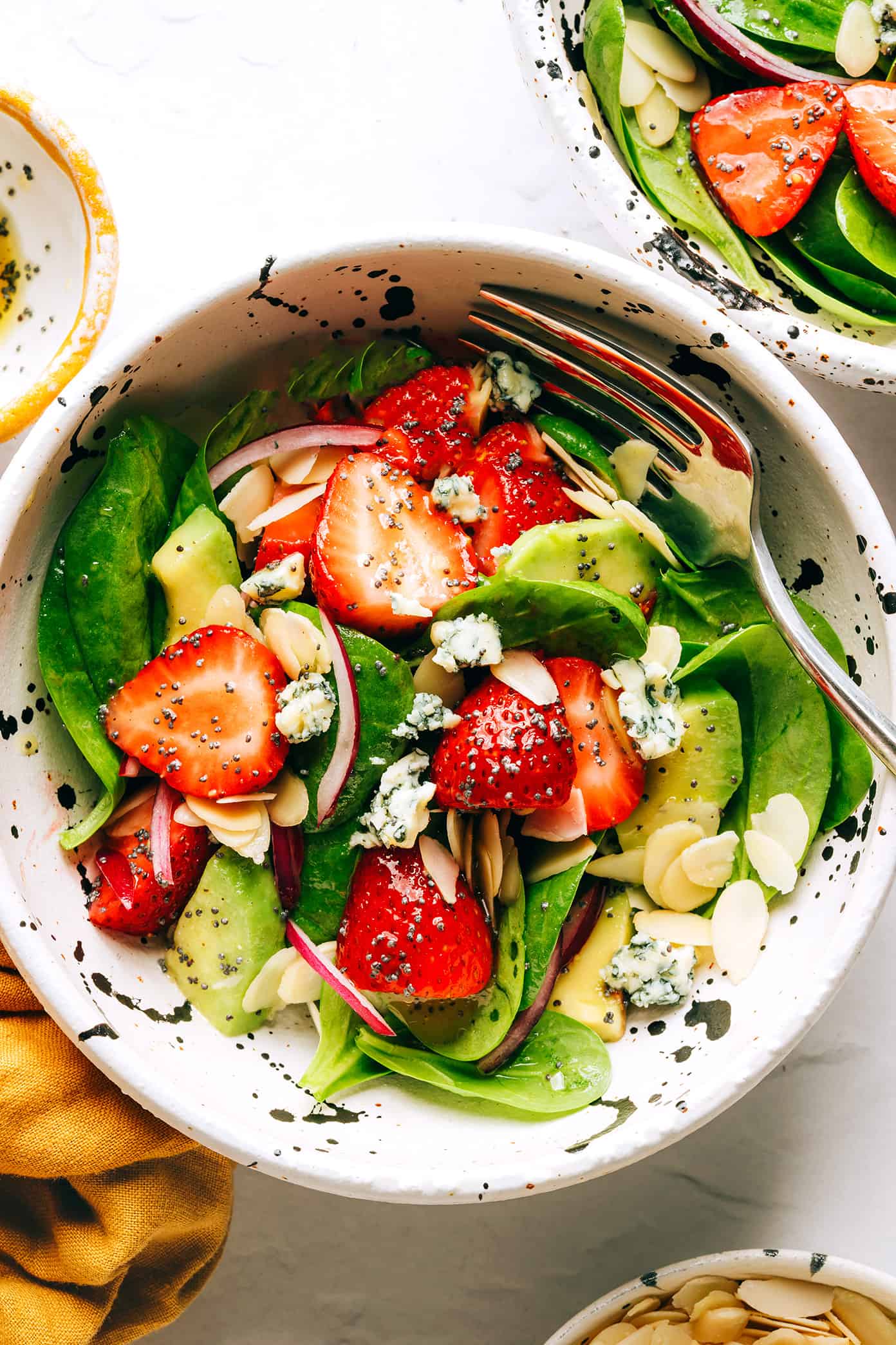 This fresh strawberry spinach salad recipe is tossed with creamy avocado, toasted almonds, sliced red onion, your choice of cheese (blue, feta, goat) and a lightly-sweetened honey poppyseed dressing. Feel free to add in some grilled chicken, shrimp or bacon if you'd like too! | gimmesomeoven.com Strawberry Spinach Salad in Bowl with Poppyseed Dressing